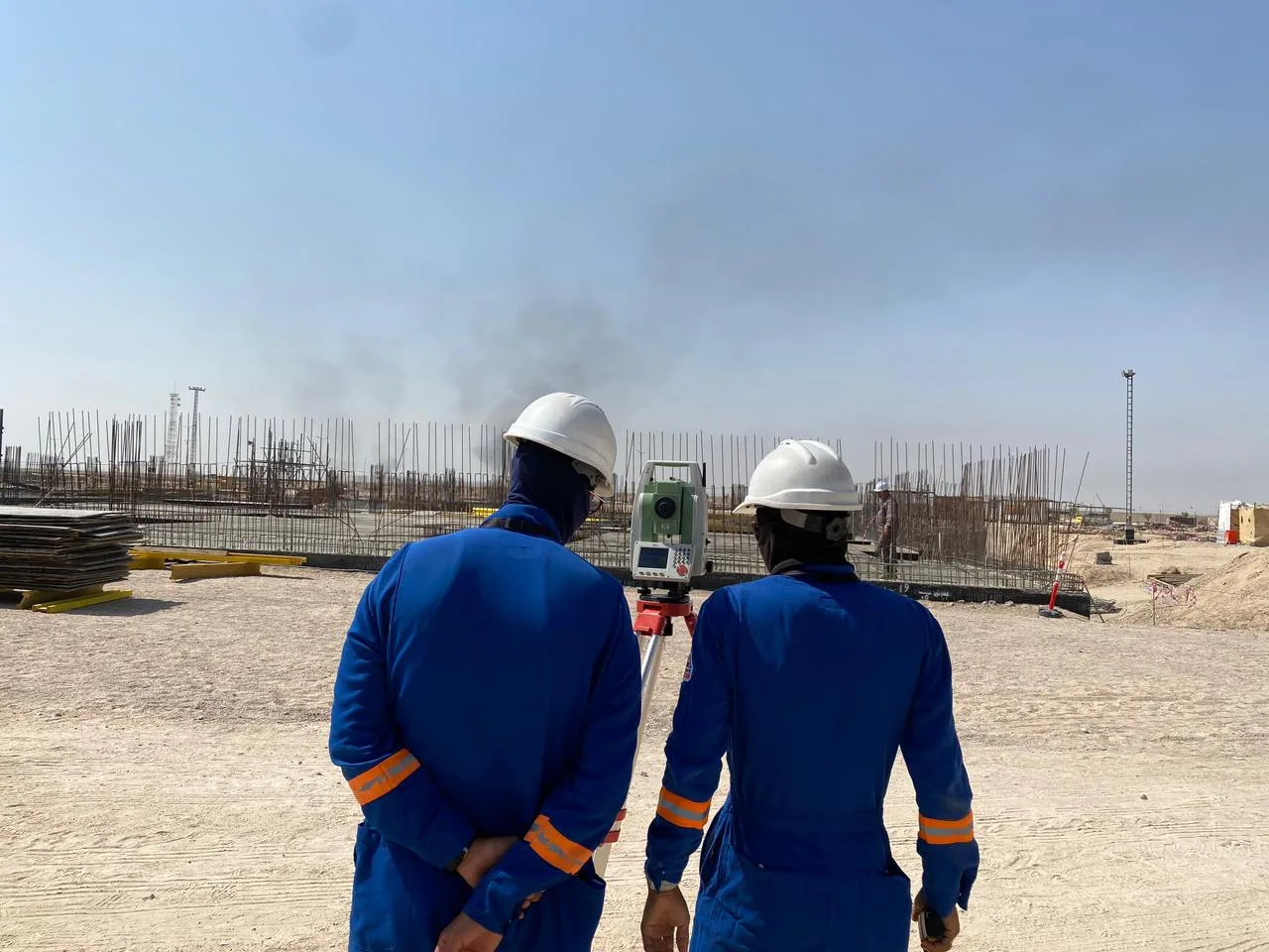 Two surveyors in safety gear reviewing total station measurements at a reinforced concrete construction site