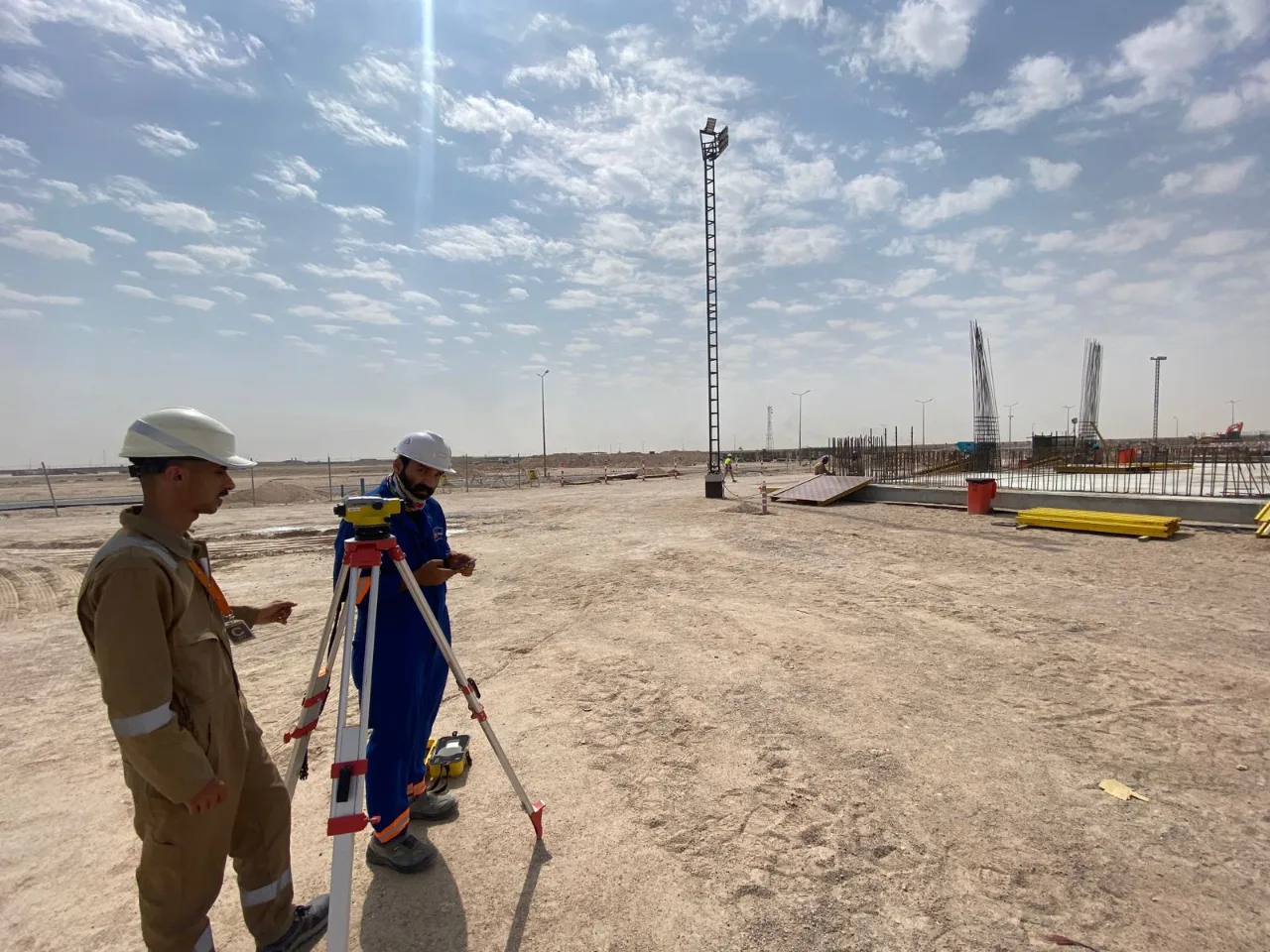 Two field surveyors operating a total station during a land survey at an industrial construction site